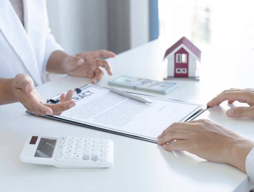 Showing home loan consultation with model house, contract, and cash stack.