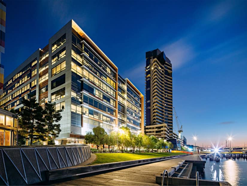 Showing illuminated modern office building near waterfront at dusk.