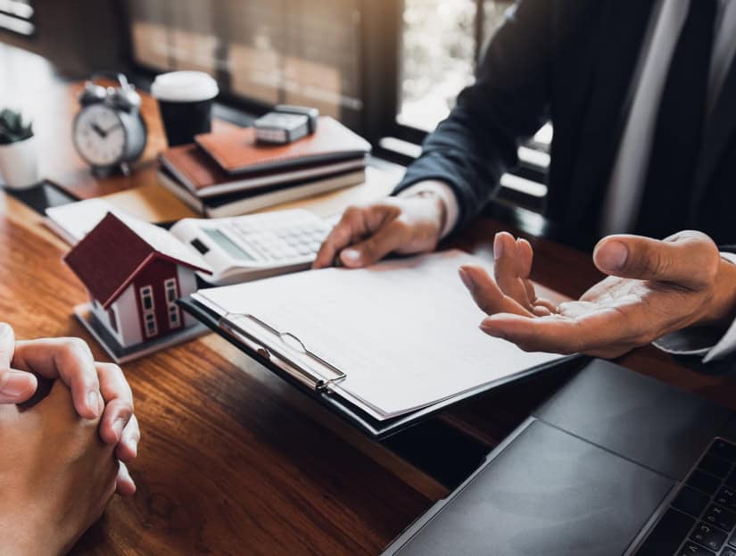 Showing hands of finance consultant with house model and documents on desk